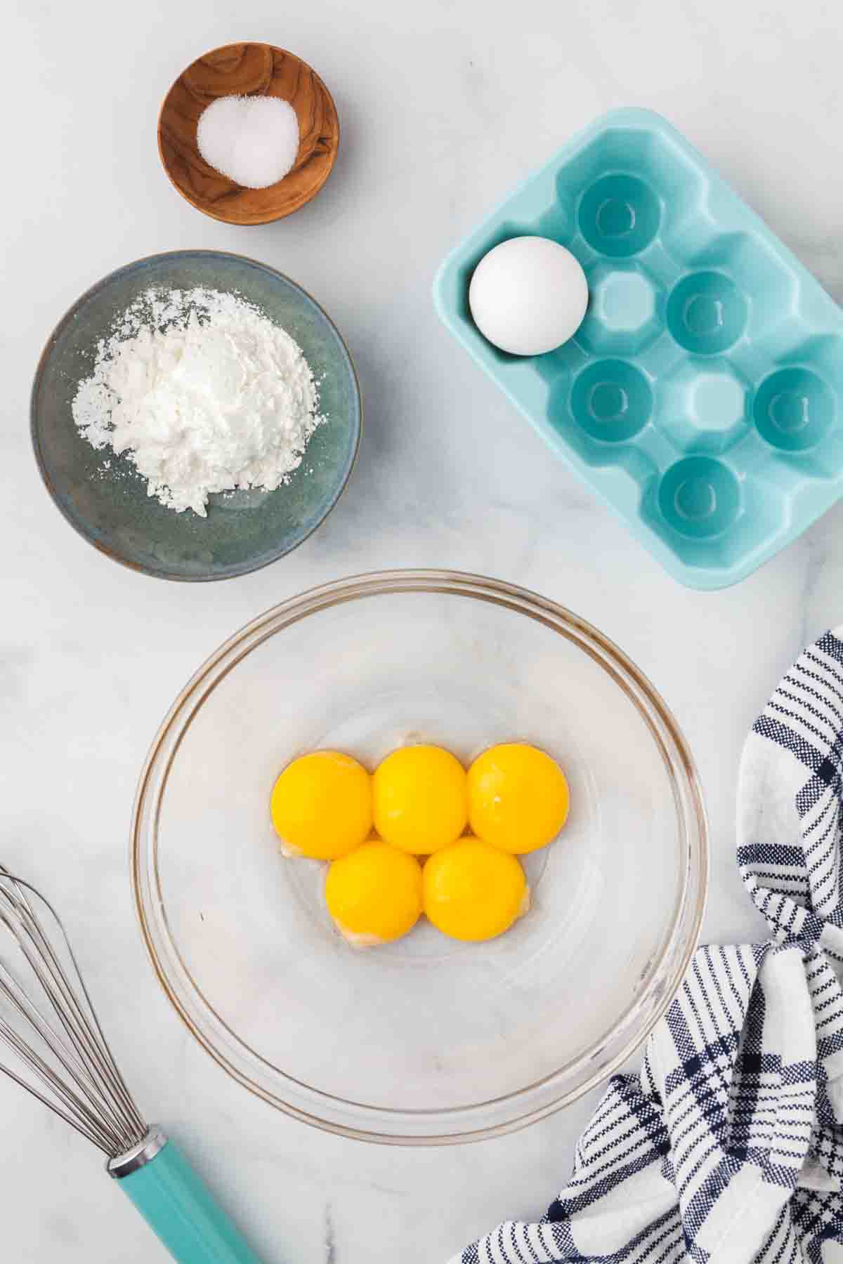 Egg yolks and sugar in a glass mixing bowl.