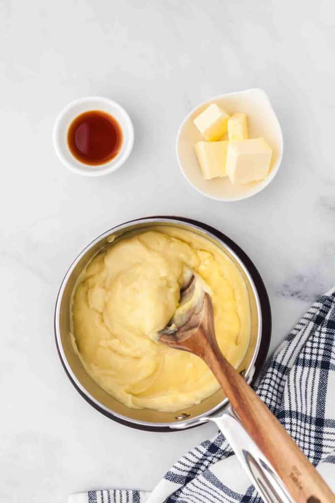 Pastry cream in a saucepan with bowls of butter and vanilla nearby.