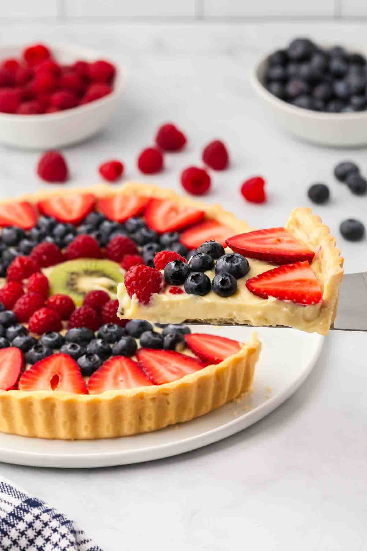 A slice of fruit tart being  lifted from the serving plate.