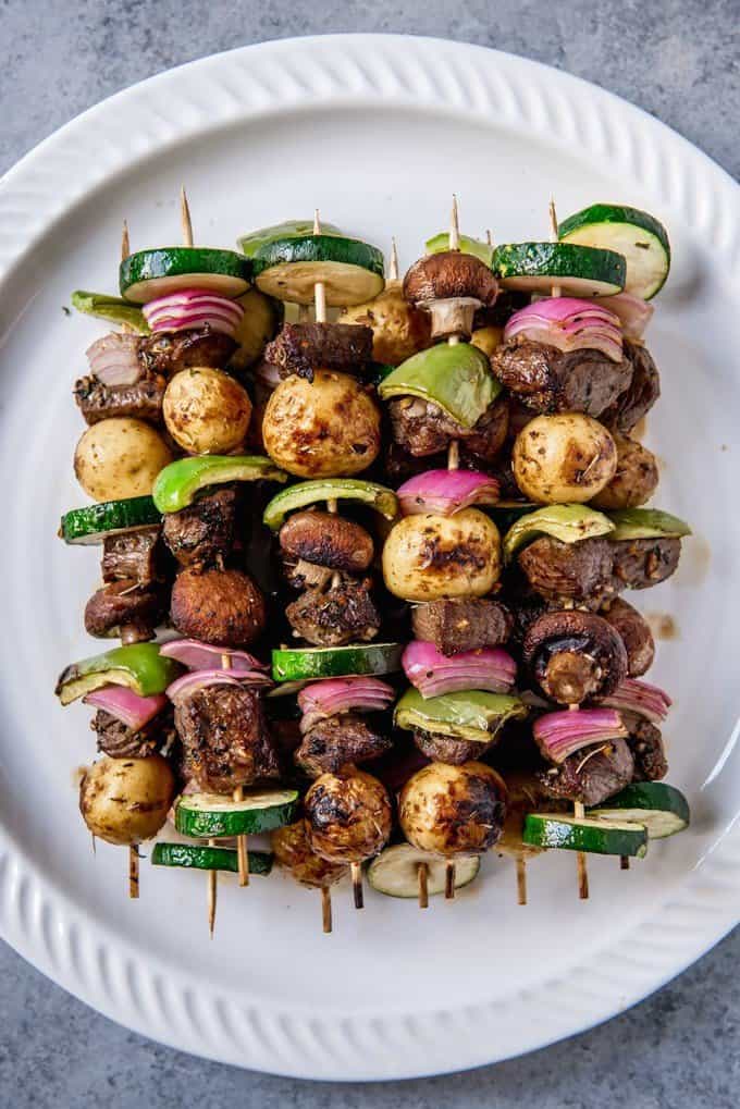 An image of steak skewered on wooden skewers with zucchini, onions, peppers, mushrooms and potatoes for marinated beef shish kabobs.
