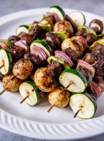 potaotes, beef, and veggies skewers on wooden sticks and resting in a neat pile on a white plate