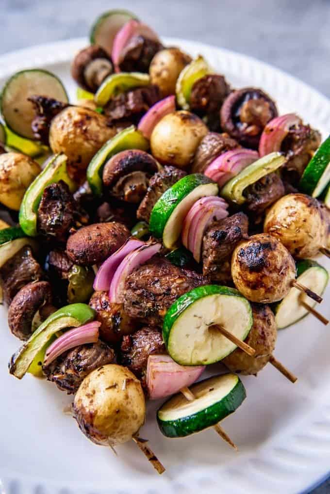An image of a plate of grilled marinated steak kebabs with zucchini, potatoes, mushrooms, peppers, and onions.