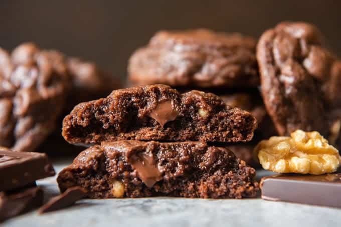 An image of a chocolate cookie with melted chocolate and walnuts inside, broken in half and stacked on top of each other.