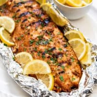 grilled salmon in a bed of foil on a white plate with lemon slices all around it