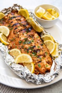grilled salmon in a bed of foil on a white plate with lemon slices all around it