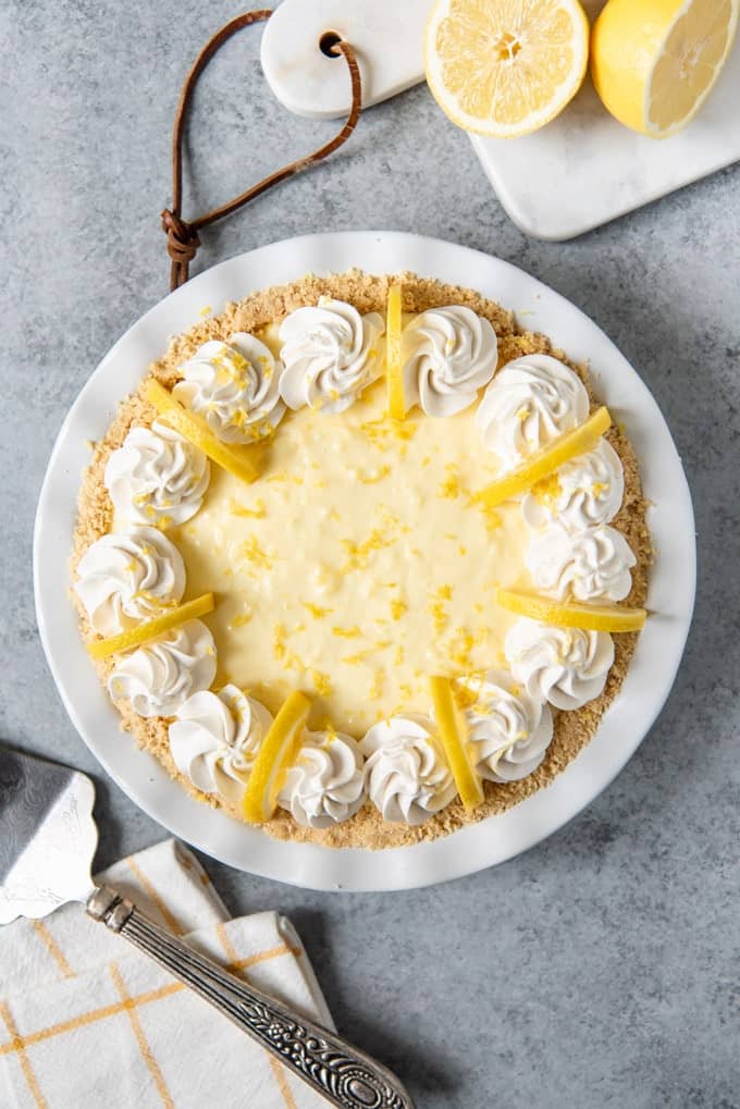 An image of an entire no-bake lemon cream pie decorated with swirls of whipped cream and lemon wedges.