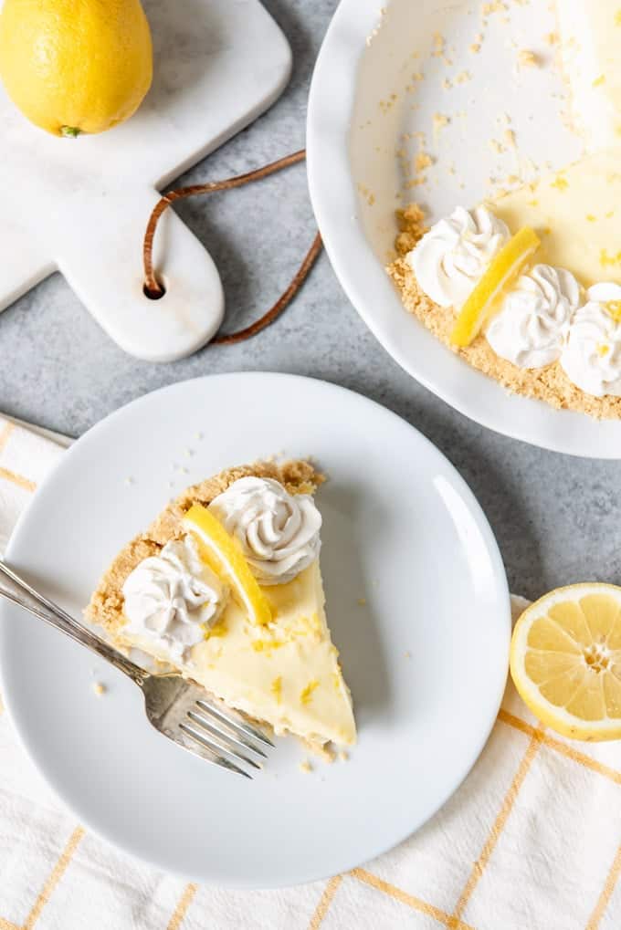 Un'immagine di una fetta di torta al limone senza cottura su un piatto bianco accanto al piatto della torta.