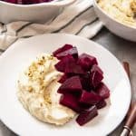 An image of a plate of pantzaria me skordalia, a tradition Greek dish made with roasted beets and a garlic-potato spread, sprinkled with pistachios.