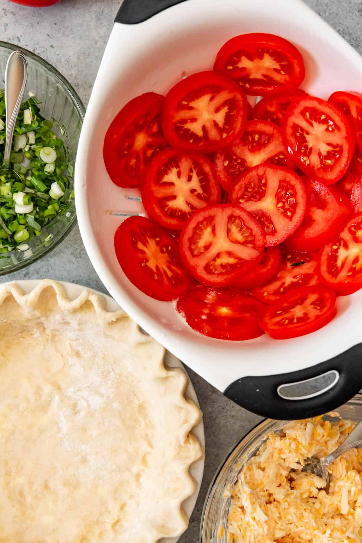 An image of the ingredients for a tomato pie - pie crust, tomatoes, cheese, mayo, green onions, and basil.