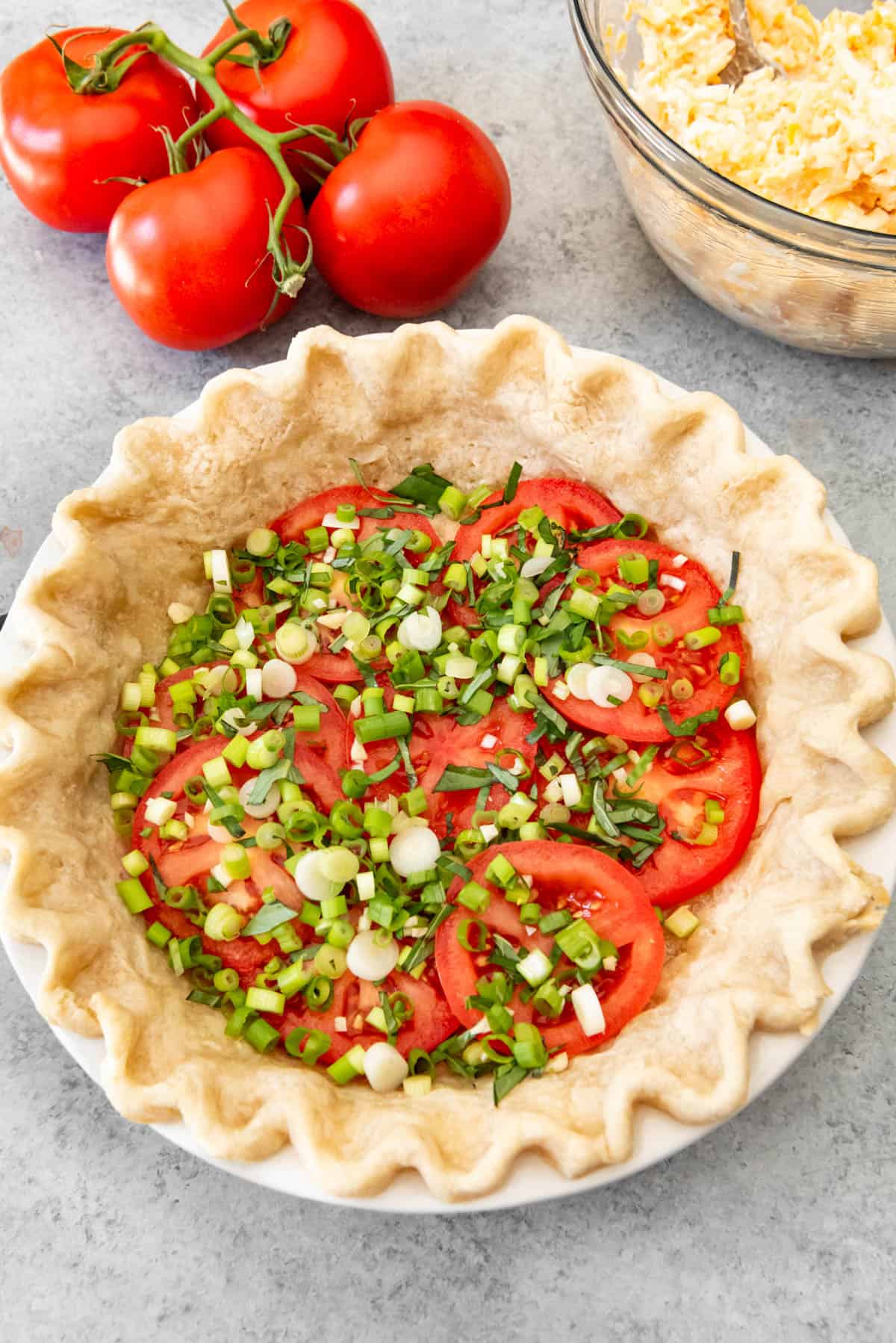 A layer of sliced tomatoes and green onions in a parbaked pie crust.