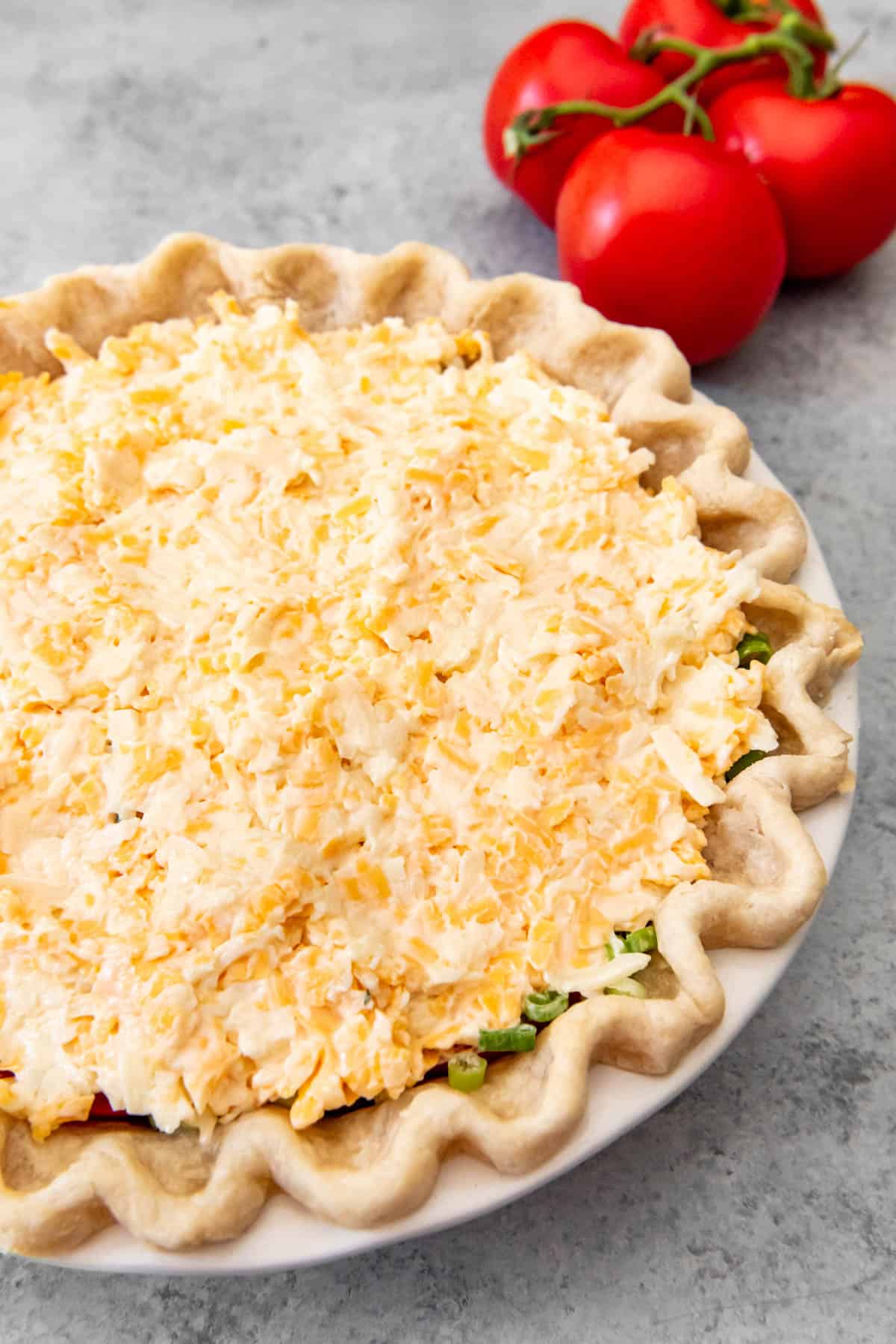 A layer of mayonnaise and shredded cheese on top of a tomato pie before baking.