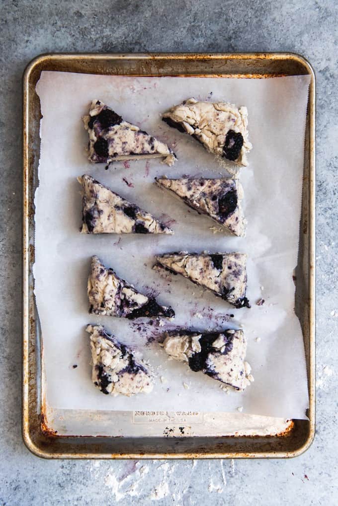 An image of a baking sheet with triangle-shaped blackberry scones on it, ready to go into the oven to bake.