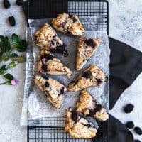 an aerial view of blackberry scones on wax paper on a wire rack with fresh flowers and berries to the side