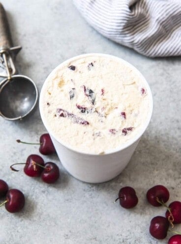 An image of a container of cherry vanilla ice cream with fresh sweet cherries next to it.