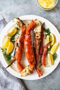 an aerial view of a plate filled with cooked crab legs and garnished with lemon slices and fresh herbs