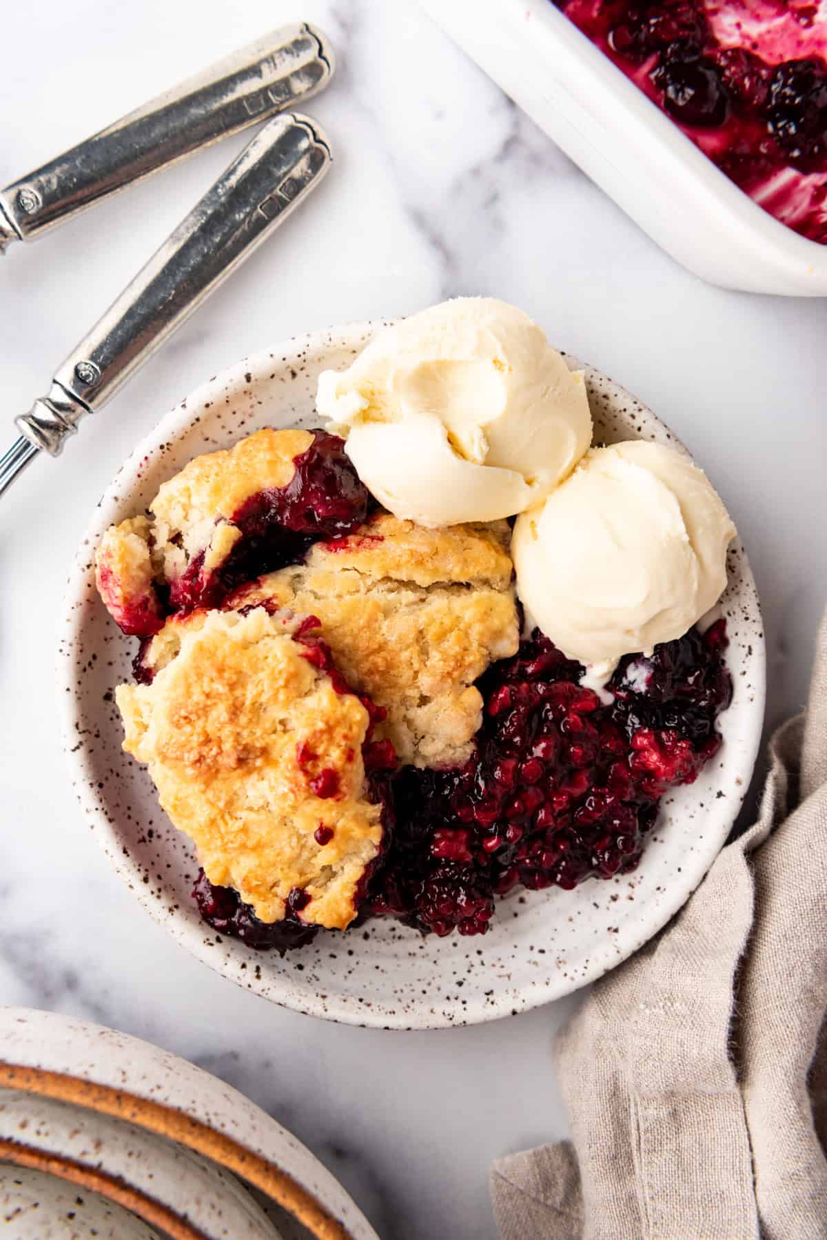 An overhead image of a plate of mixed berry cobbler with two scoops of vanilla ice cream.