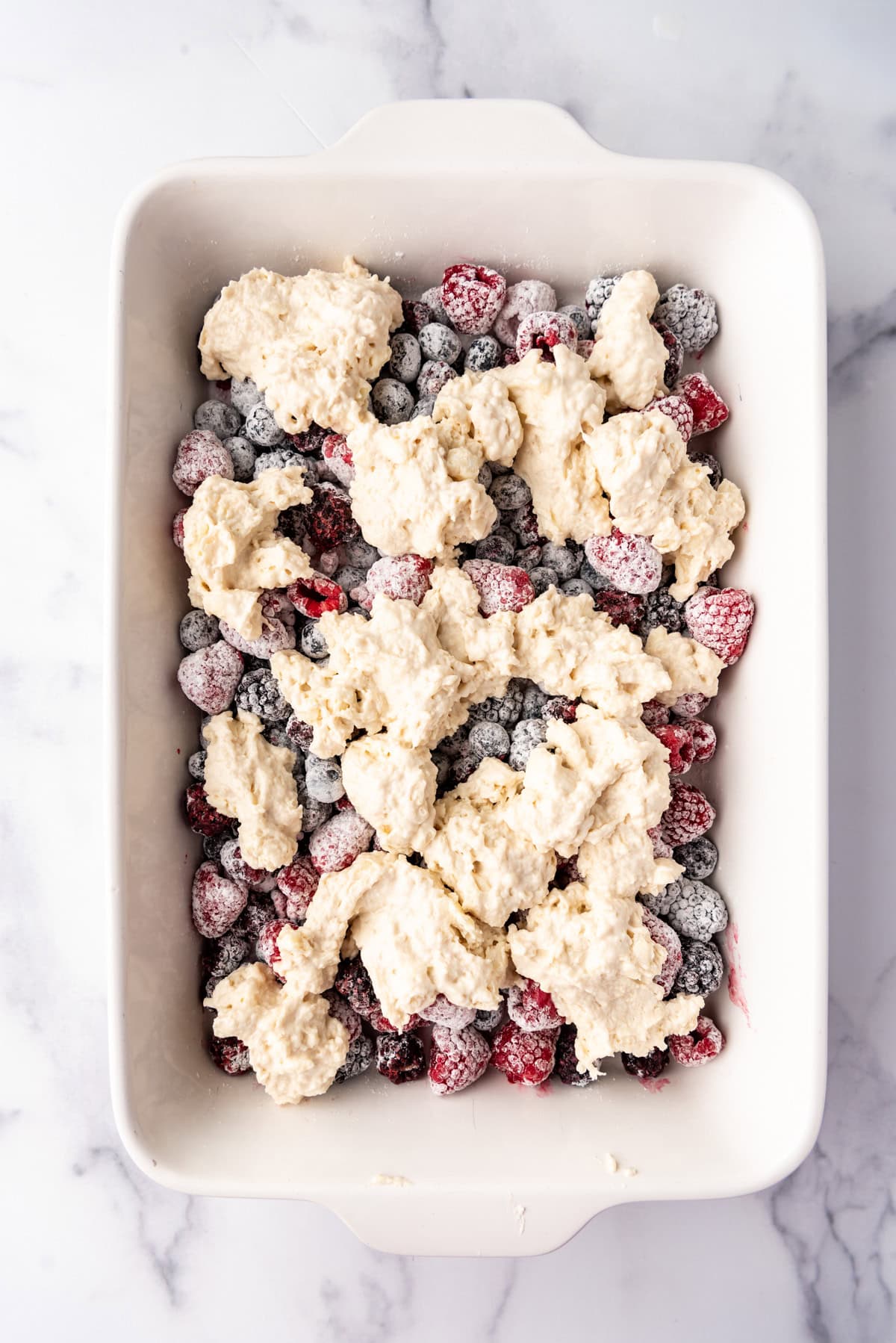 Adding cobbler topping to mixed berries and sugar in a bowl.