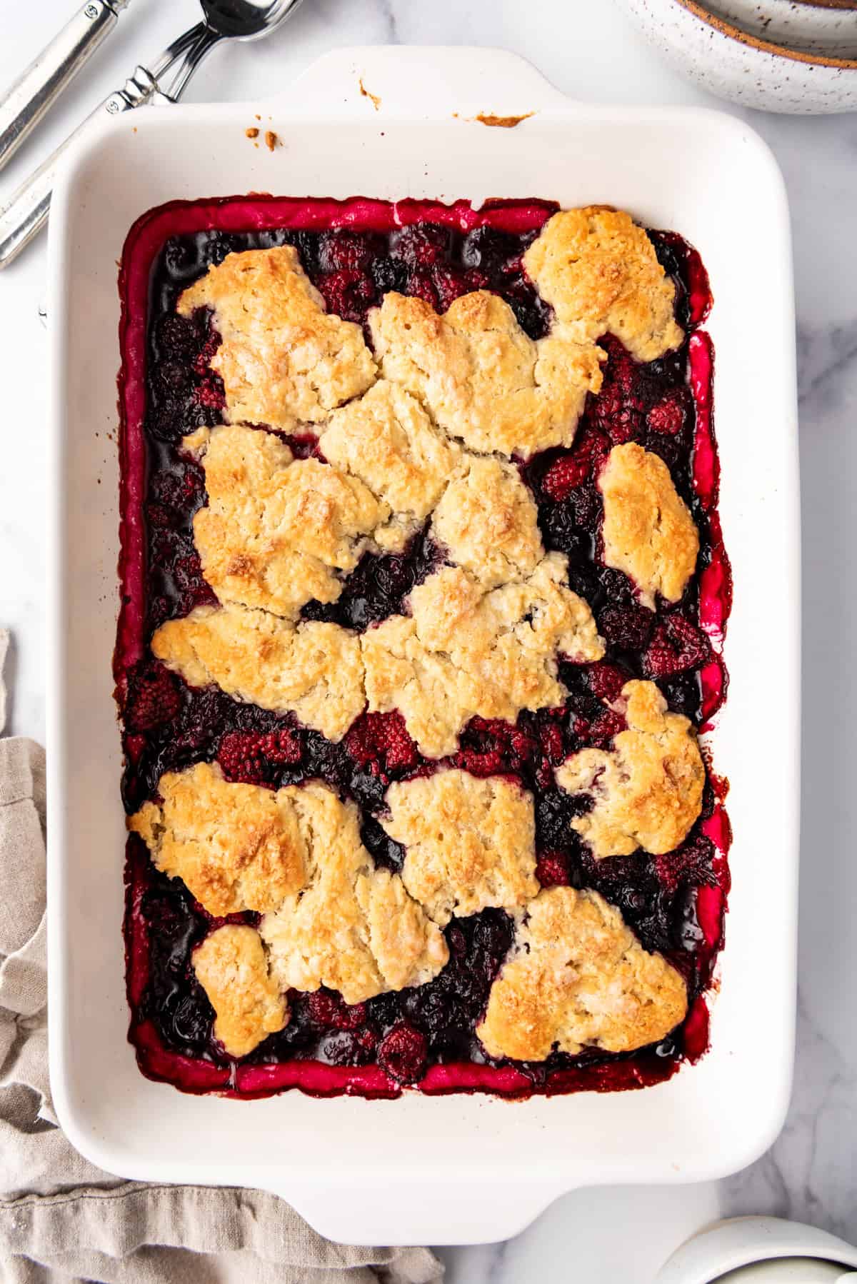 A baked mixed berry cobbler in a white baking dish.