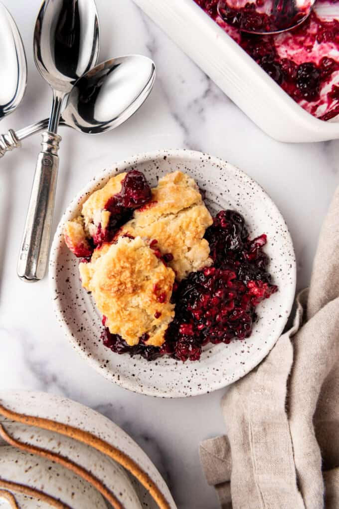 An overhead image of a plate of mixed berry cobbler next to some spoons and a linen napkin.