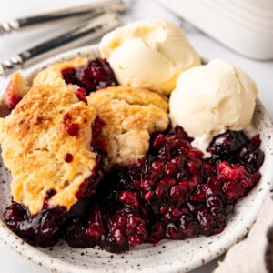 An image of a serving of mixed berry cobbler on a plate with vanilla ice cream.