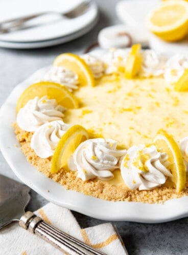 A no bake sour cream lemon pie in a white pie plate garnished with whipped cream and lemon slices.