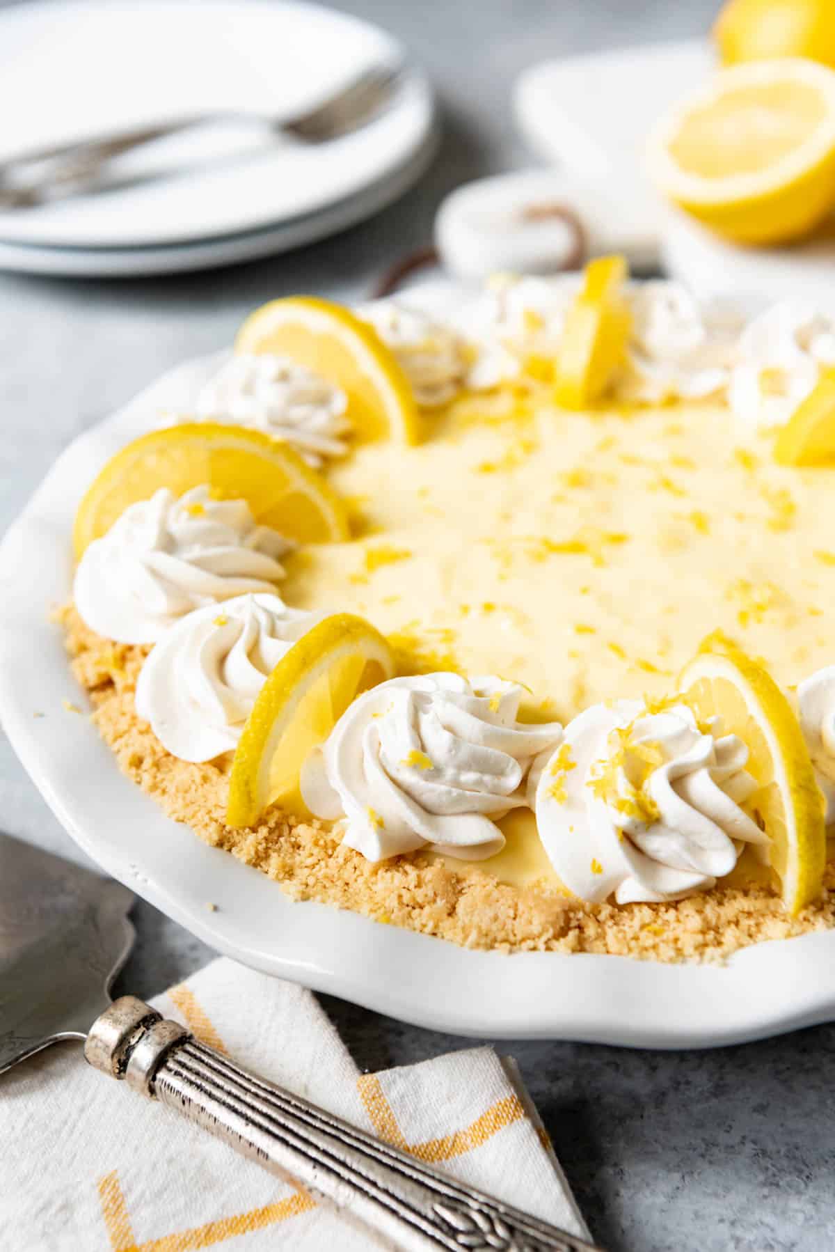 A no bake sour cream lemon pie in a white pie plate garnished with whipped cream and lemon slices.