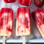 strawberry pineapple coconut popsicles on a baking dish filled with ice and scattered strawberries
