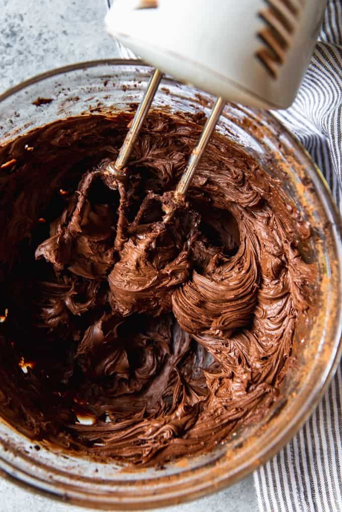 electric mixers in a glass bowl with chocolate frosting