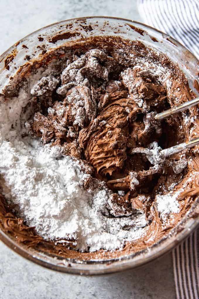 An image of powdered sugar being mixed into a bowl of chocolate frosting.