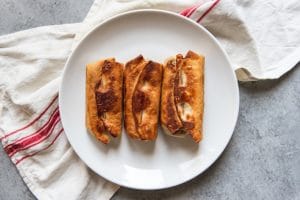 the bottoms of three cooked Chimichangas on a white plate