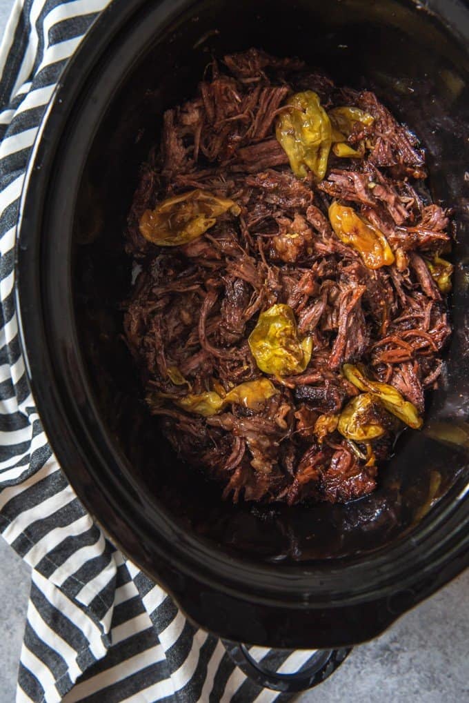 An image of shredded Mississippi Pot Roast in the slow cooker with pepperoncinis.