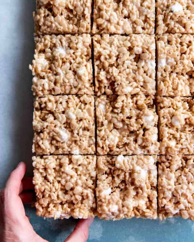 An image of a hand reaching for a salted brown butter rice krispie treat square.