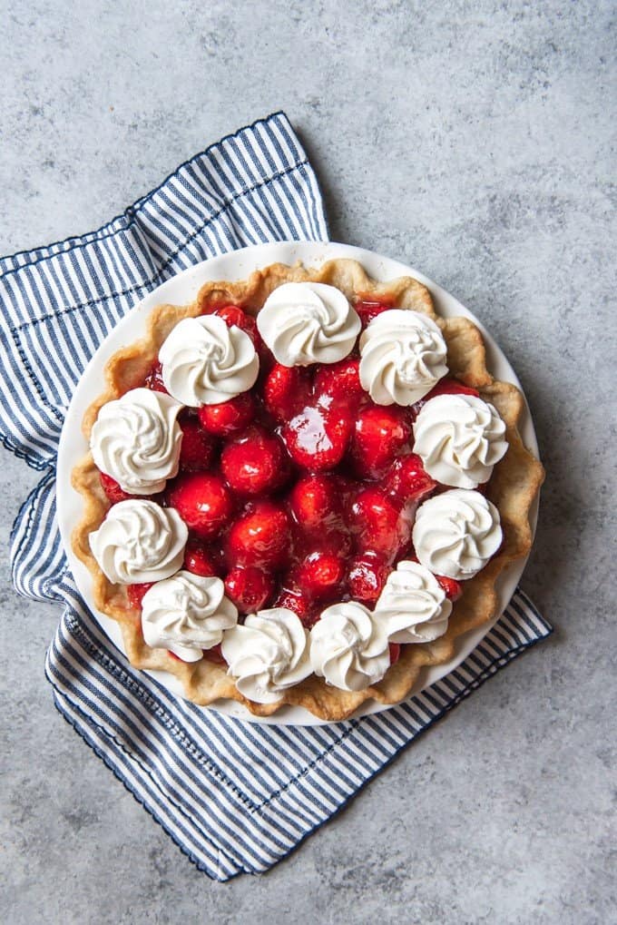 An image of a homemade strawberry pie topped with dollops of fresh whipped cream.