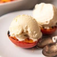 grilled peaches topped with vanilla ice cream on a white plate