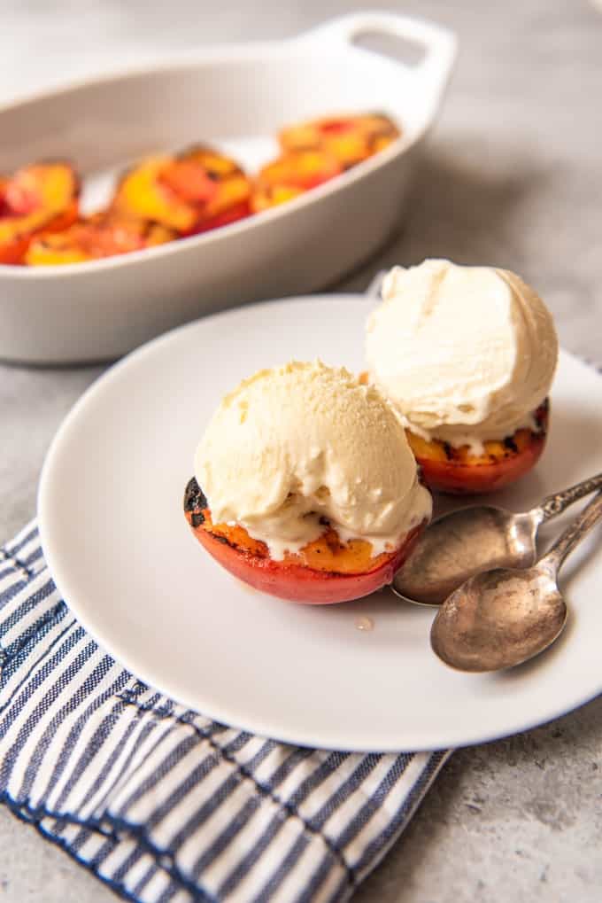 two grilled peaches with ice cream on top on a white plate with two spoons