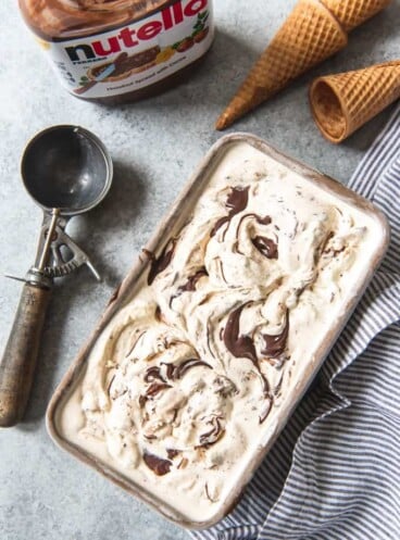 chocolate hazelnut swirl ice cream in a pan next to cones, a scooper and a jar of Nutella