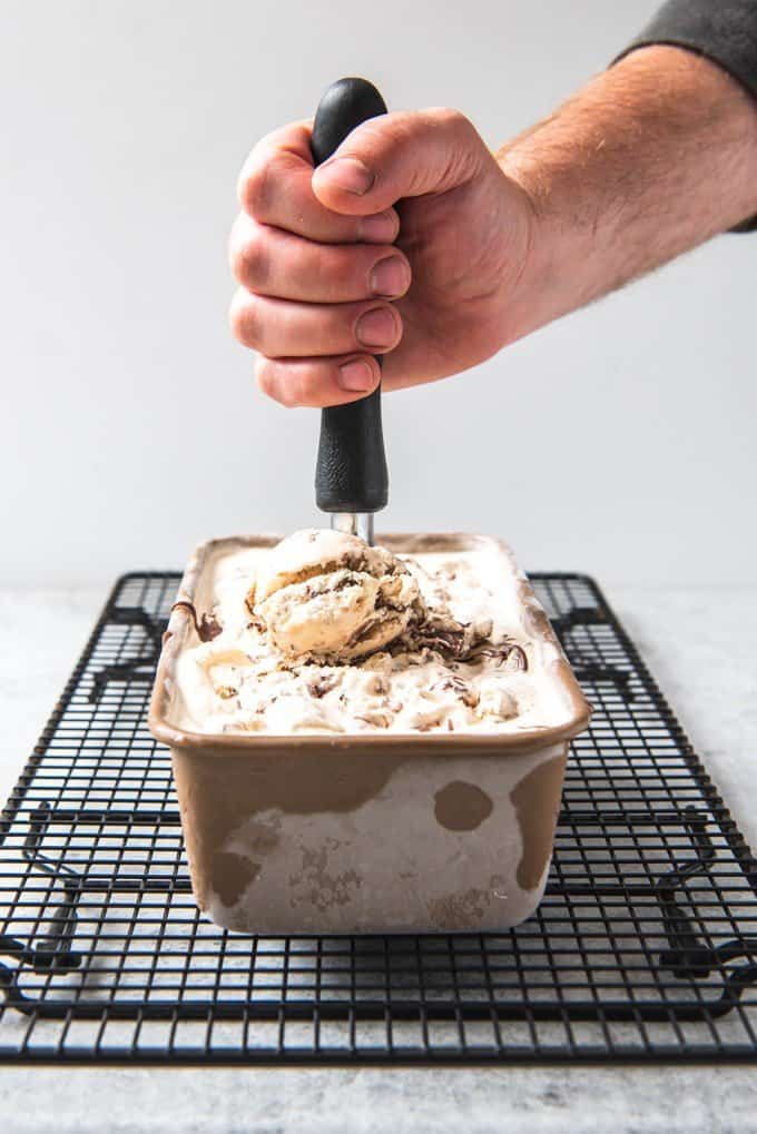 An image of a hand holding an ice cream scooper and scooping Nutella Swirl Gelato from the container it cured in.