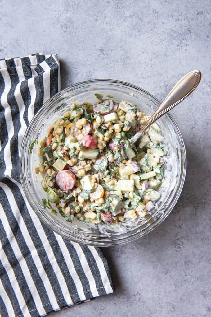 An image of a creamy summer corn salad made with cherry tomatoes, cucumbers, cilantro, and lime juice, and lots of fresh grilled corn.