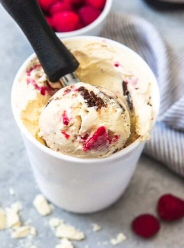 White Chocolate Raspberry Truffle Ice Cream in a white container with an ice cream scoop inside