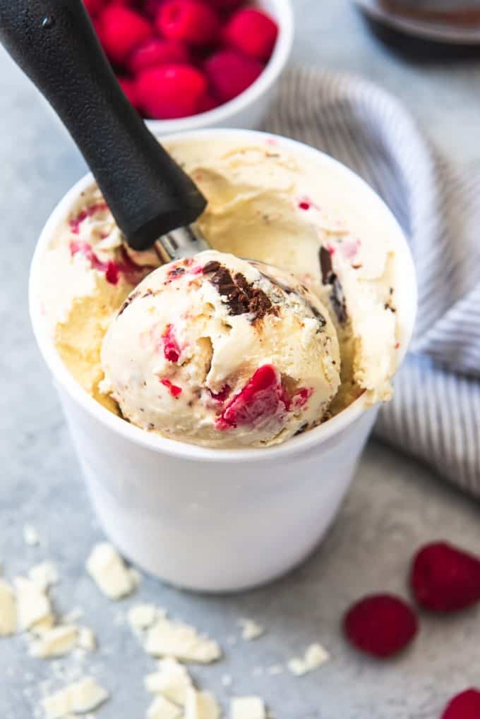 An image of a container of white chocolate ice cream with a raspberry ripple and chunks of chocolate truffles, with a big scoop scooped out on the top. 