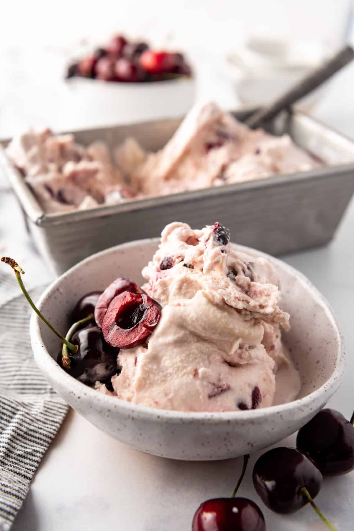 A bowl of black cherry ice cream in front of the ice cream container.