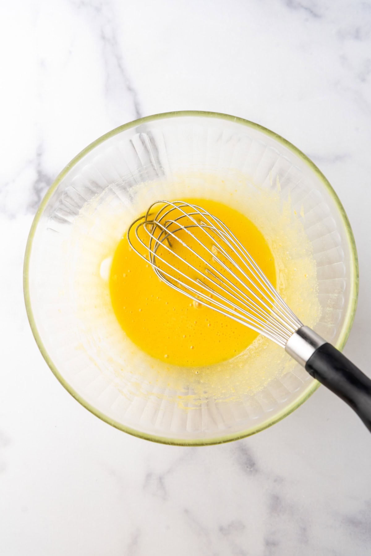 Whisked egg yolks and sugar in a glass bowl with a whisk.