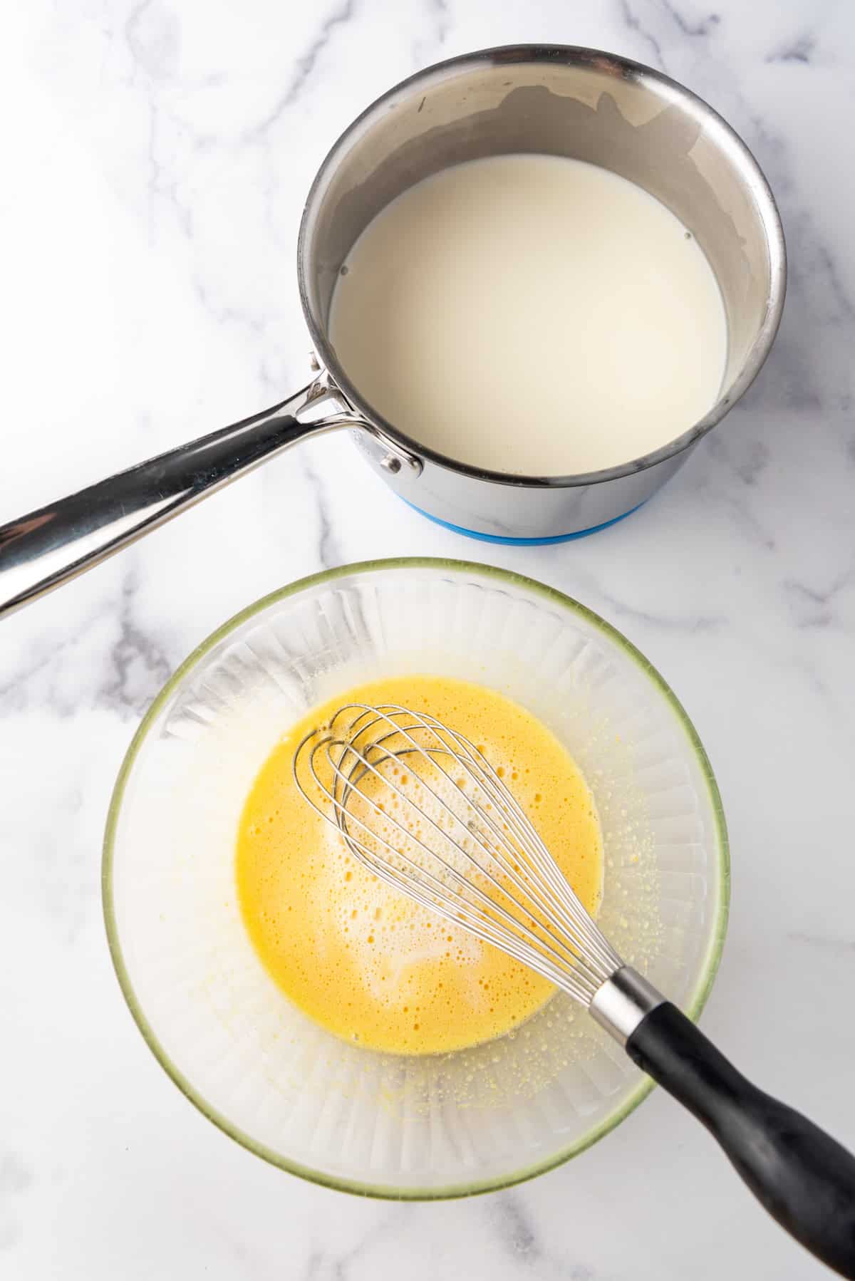 Tempering eggs with hot milk mixture in a bowl.