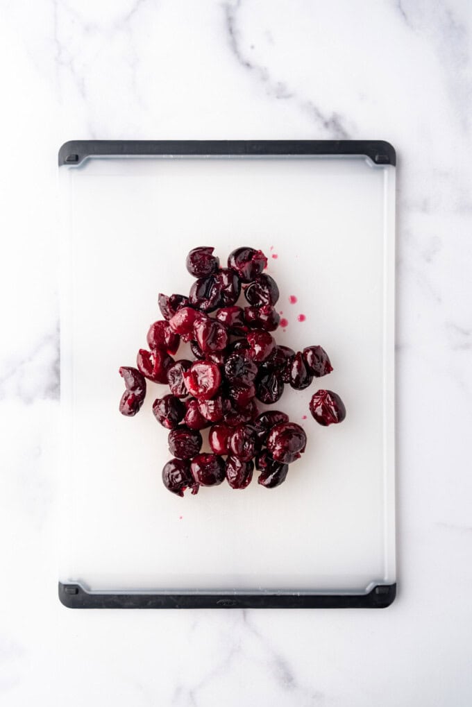 Poached, pitted cherries on a cutting board.