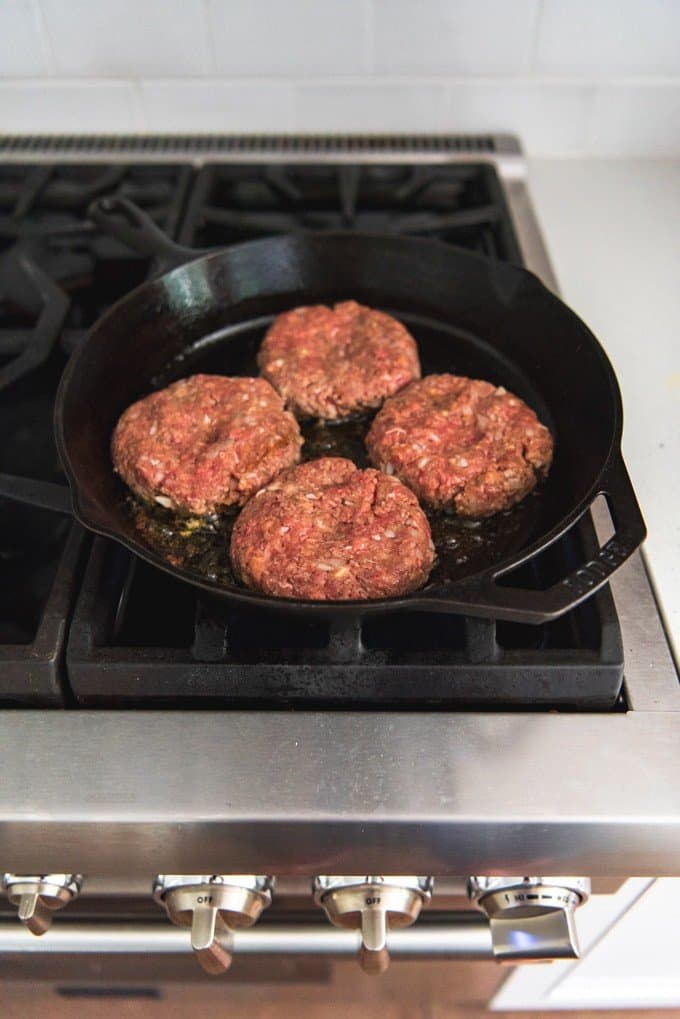 An image of four meatloaf patties pan-frying in a skillet on the stove.