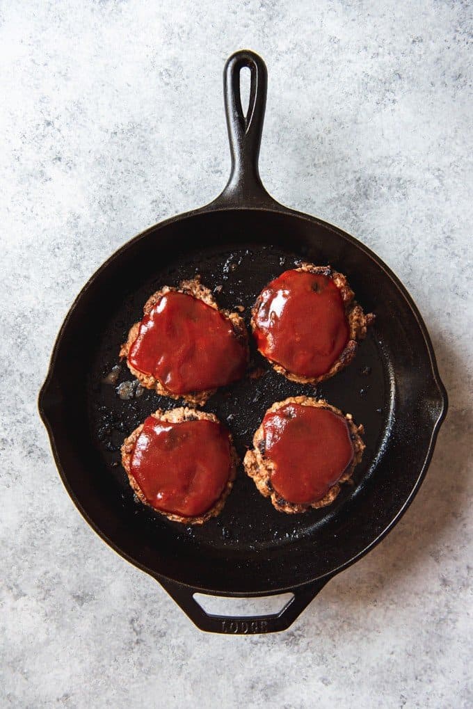 An image of four meatloaf patties pan-fried in a skillet and topped with a tangy, tomato ketchup and brown sugar sauce.