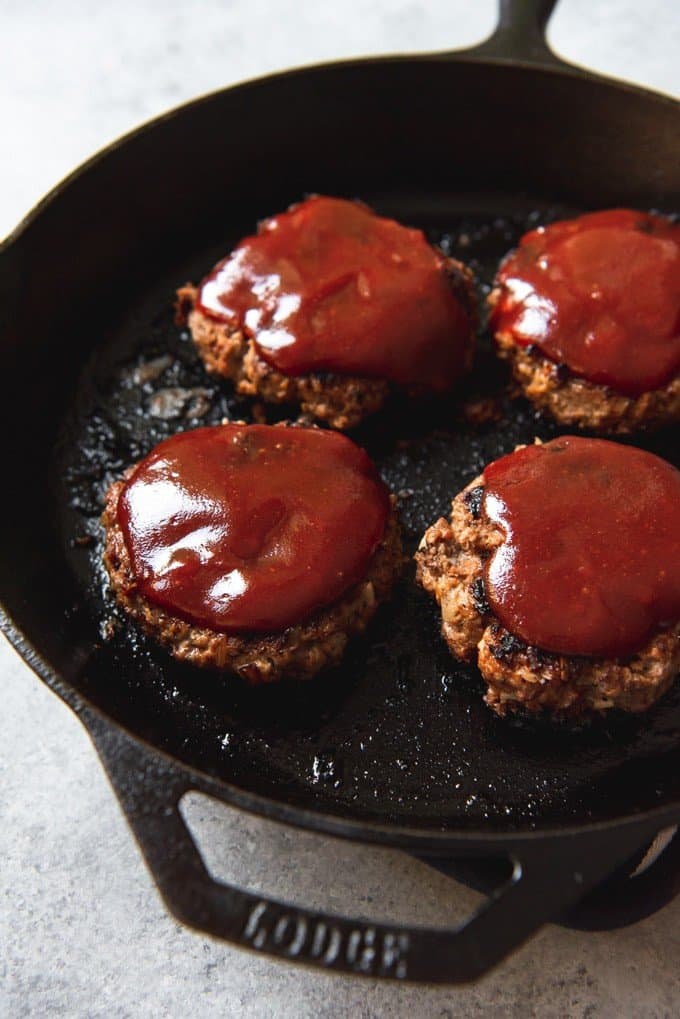 An image of four meatloaf patties in a skillet, topped with a ketchup meatloaf sauce.