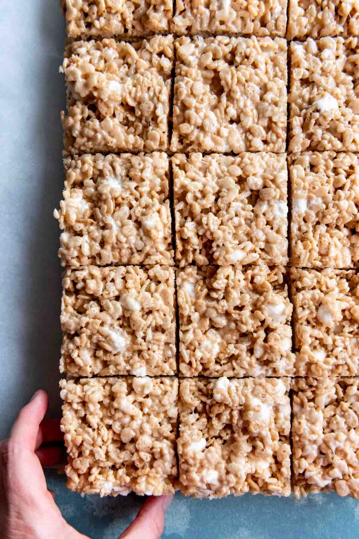 An image of a hand reaching for a salted brown butter rice krispie treat square.