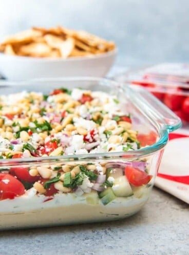 a close side view of a glass pan full of 7 layer greek dip