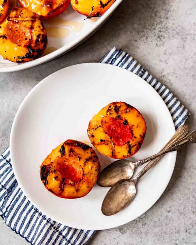 An image of two grilled peach halves on a white plate, drizzled with honey.